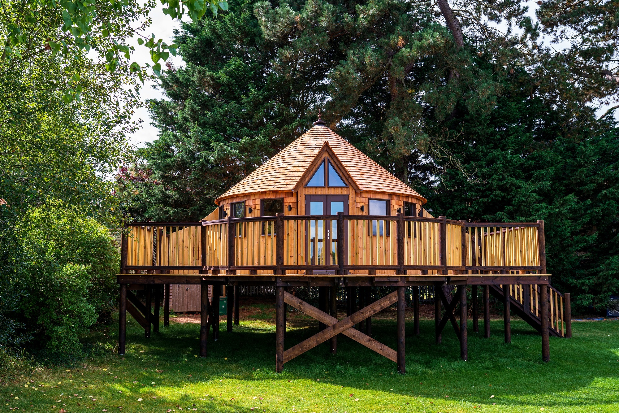 Wooden house on stilts standing on grass surrounded by trees and blossom