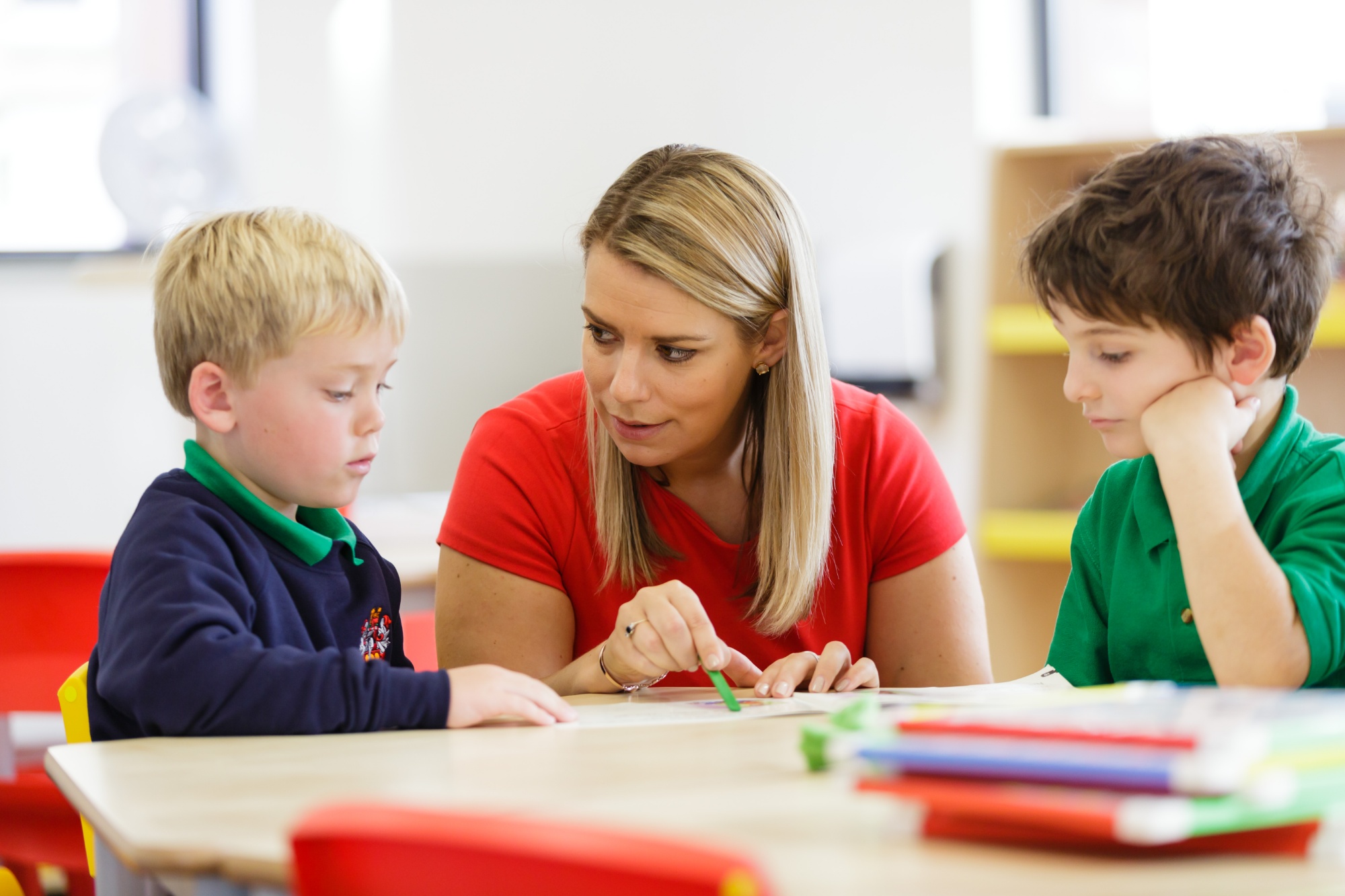 A woman instructing two children in a classroom setting.