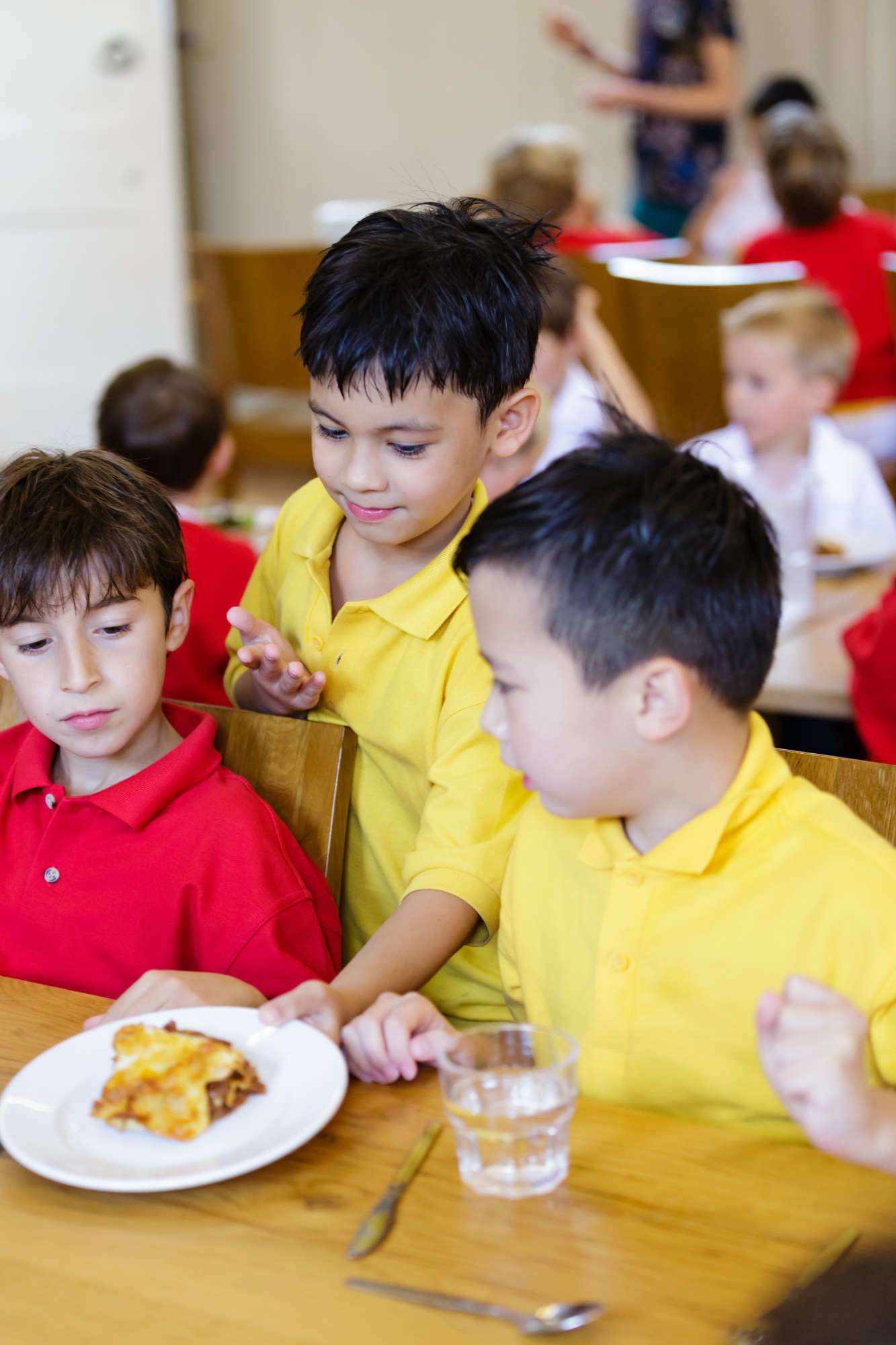 A young boy wearing a bright yellow shirt serving food to two other boys