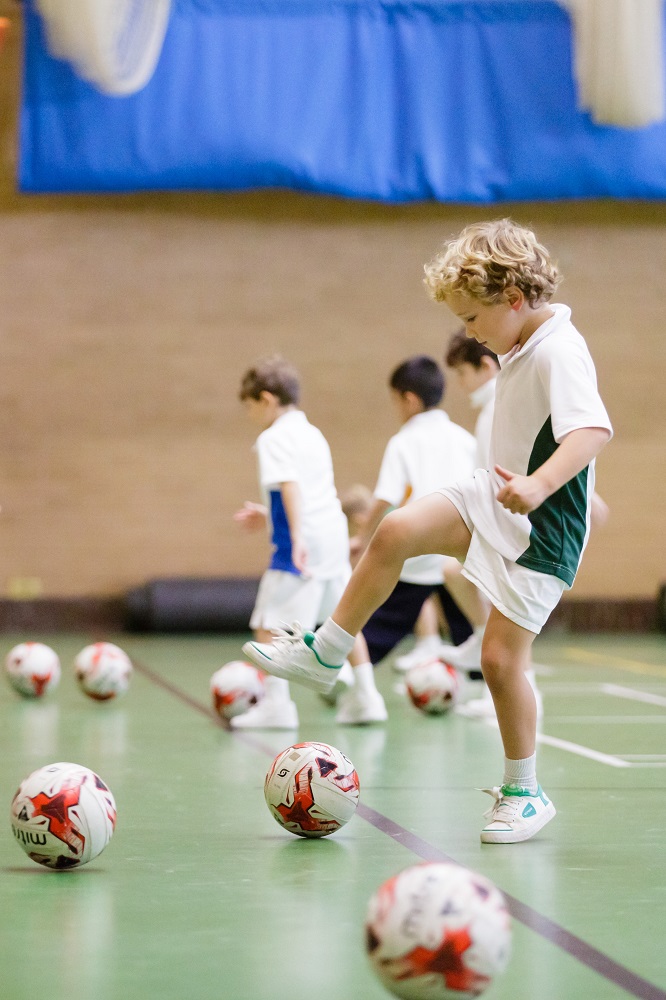 A group of young children playing football in a sports hall