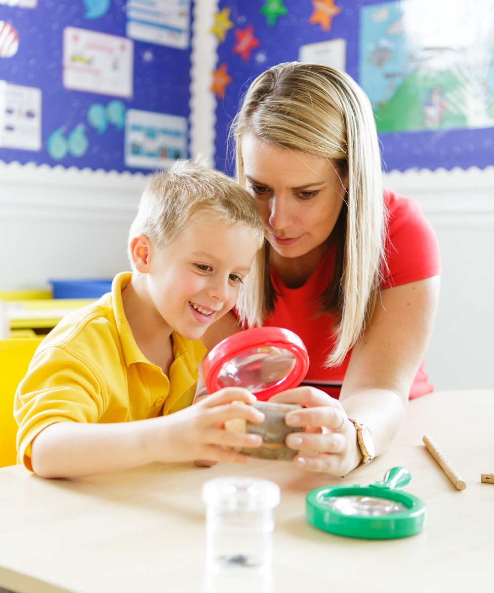 A woman and a boy examining an object through a magnifying glass closely.