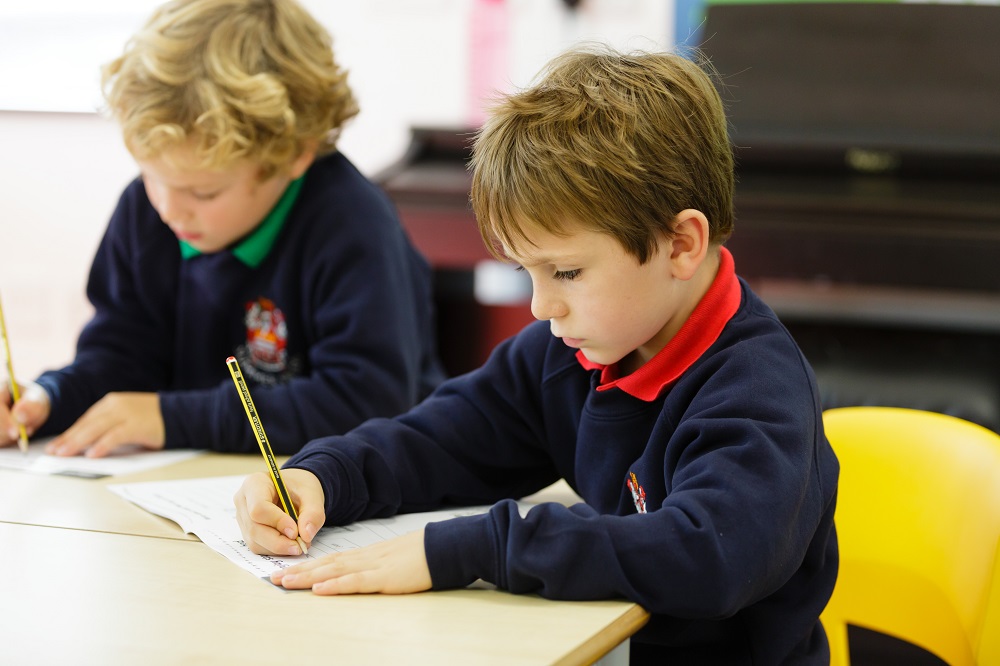 Two young boys focused on writing at a table, engrossed in their task.