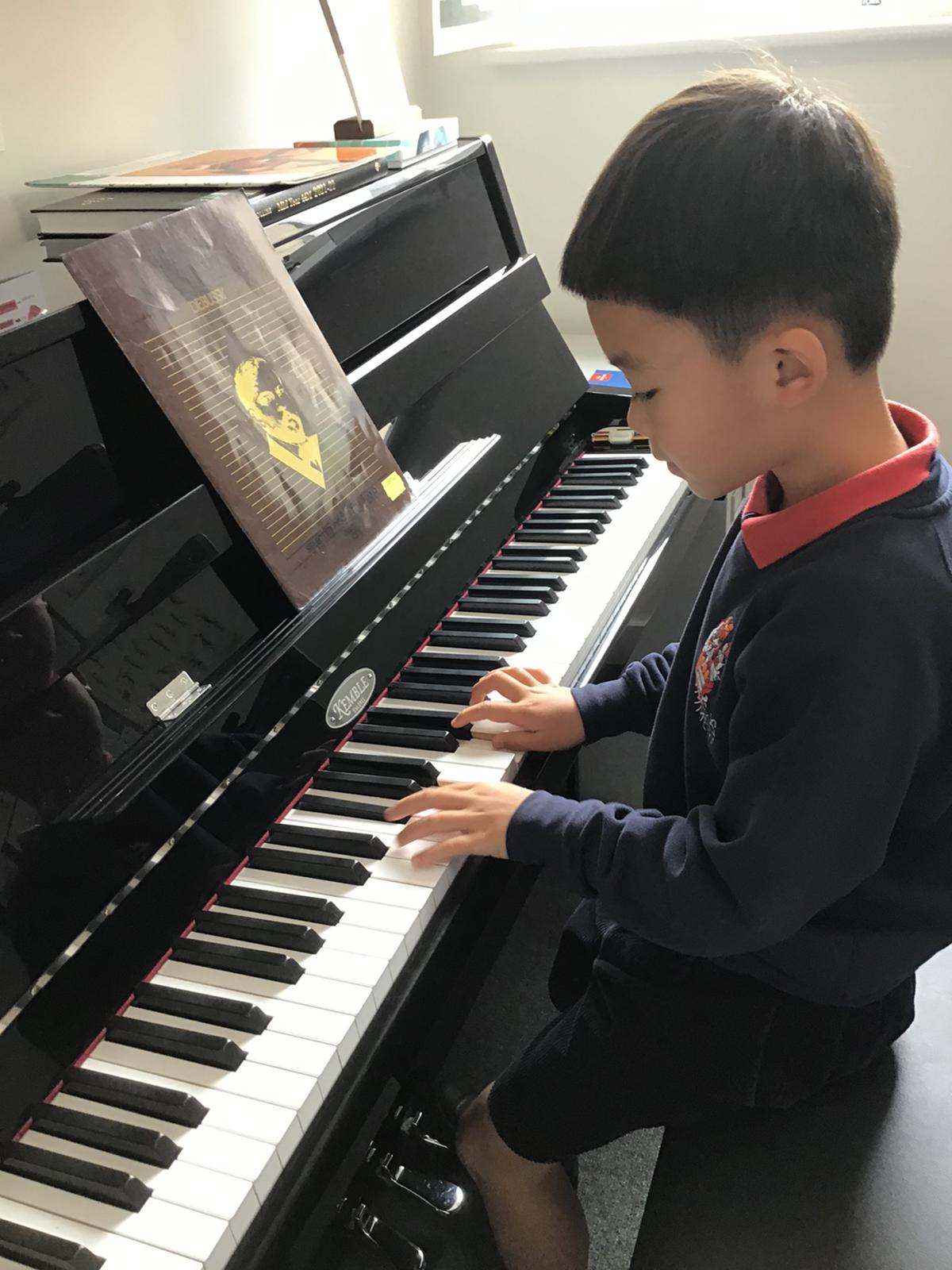 Young boy wearing Summer Fields navy school uniform playing the piano