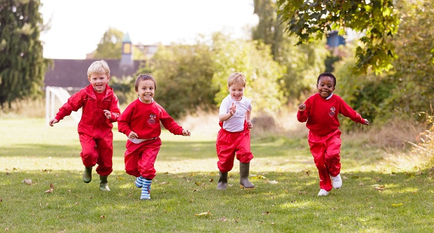 Four young boys wearing waterproofs and wellington boots running outside