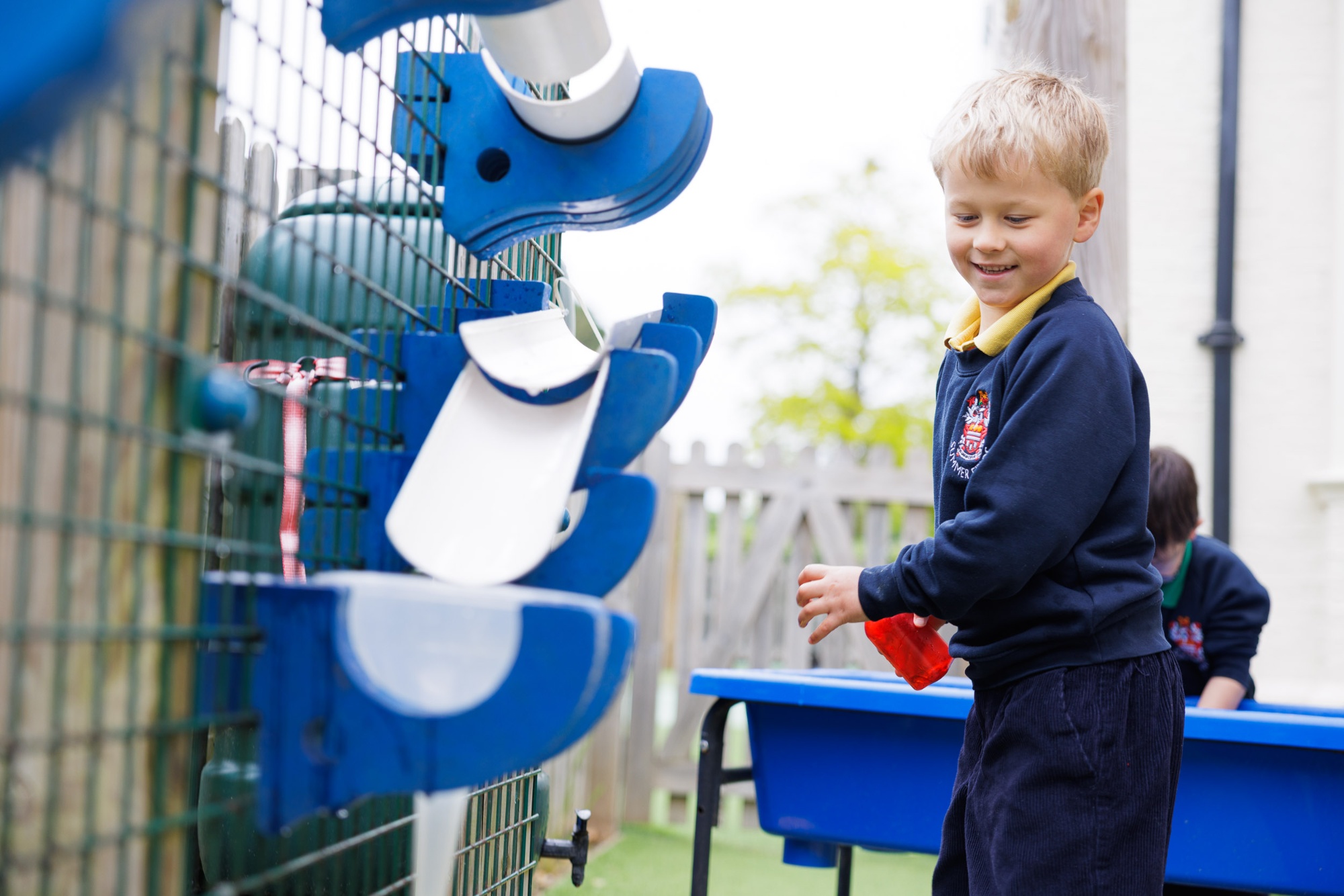 A young boy holds a metal bowl whilst playing outside.